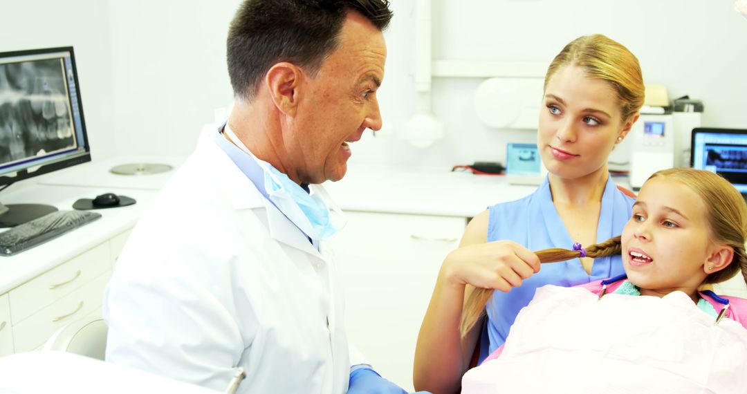 Dentist Talking with Mother While Treating Daughter in Clinic - Free Images, Stock Photos and Pictures on Pikwizard.com