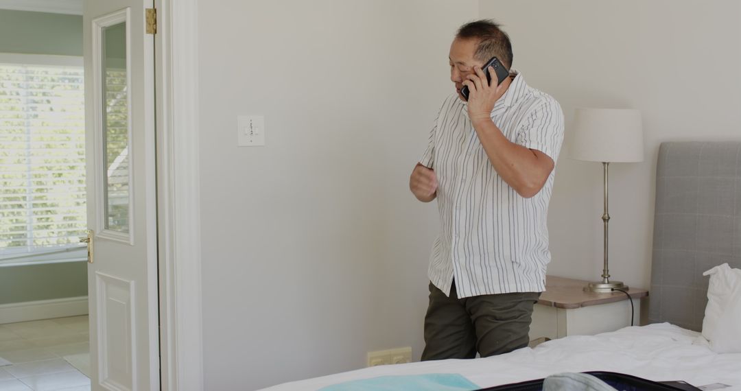 Asian Man Organizing with Phone While Packing Suitcase at Home