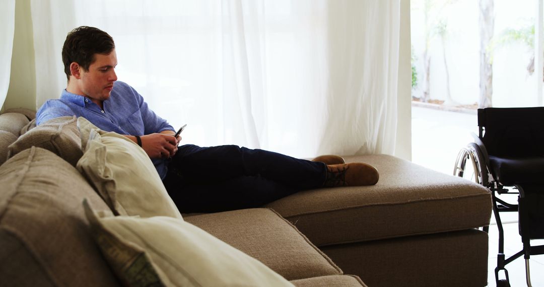 Disabled Man Relaxing on Sofa Using Smartphone - Free Images, Stock Photos and Pictures on Pikwizard.com