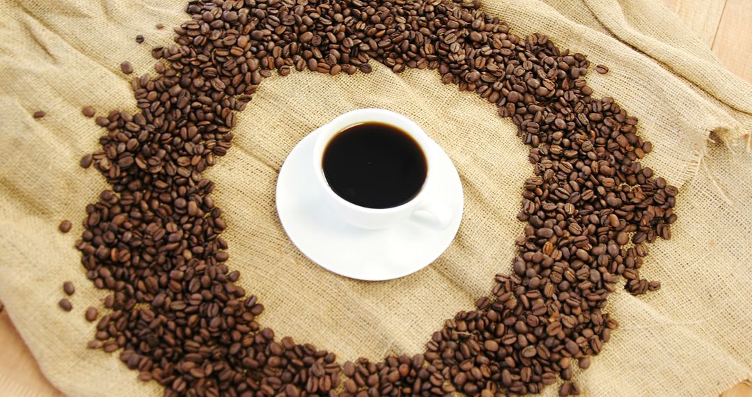 A cup of coffee sits surrounded by a circle of coffee beans on a burlap surface, with copy space - Free Images, Stock Photos and Pictures on Pikwizard.com