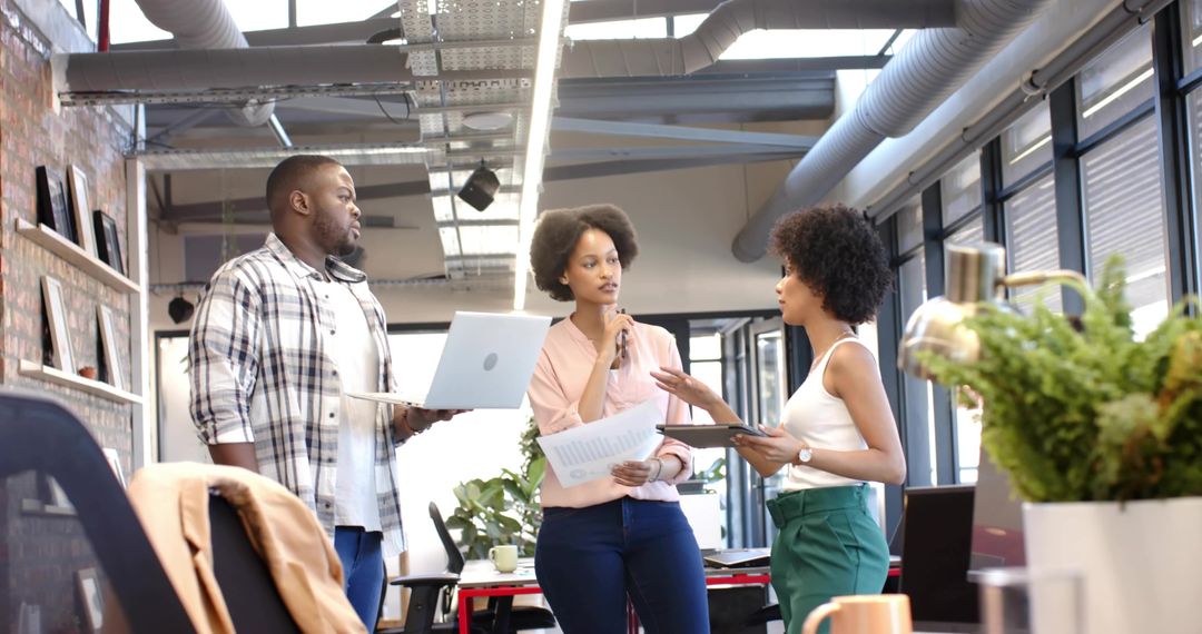 Team collaborating with laptop, tablet and reports in bright open-plan office