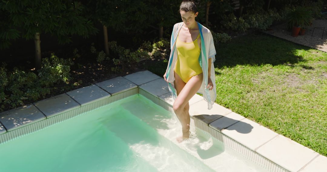 Woman Wearing Yellow Swimsuit Entering Pool in Tranquil Backyard Setting