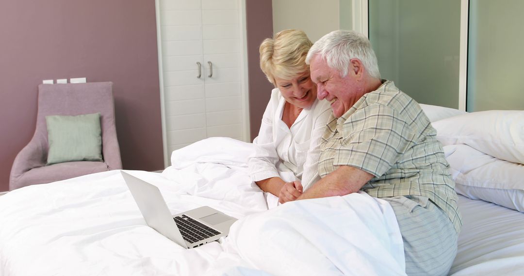 Happy Senior Couple Relaxing with Laptop in Bedroom - Free Images, Stock Photos and Pictures on Pikwizard.com