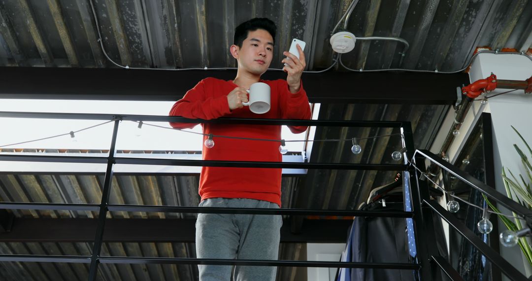 Man In Red Sweater Holding Mug And Looking At Smartphone - Free Images, Stock Photos and Pictures on Pikwizard.com