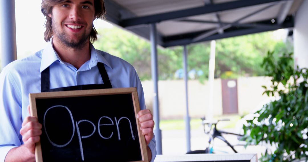 Smiling Waiter Showing Open Sign at Outdoor Cafe
