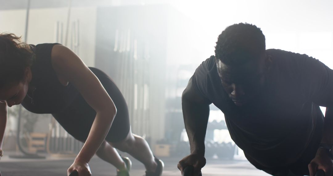 Focused Pair Intensively Exercising with Pushup Bars at Gym