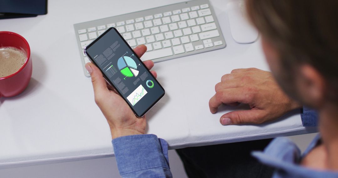 Man Analyzing Statistics on Smartphone at Desk