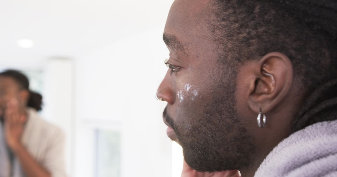 African American man applying facial cream at mirror during skincare routine