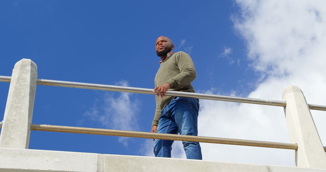 Confident Man Standing on Balcony Against Blue Sky