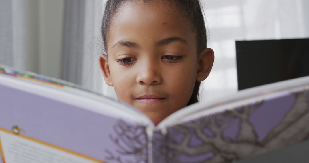 Young Girl Reading Book with Focused Expression at Home - Free Images, Stock Photos and Pictures on Pikwizard.com