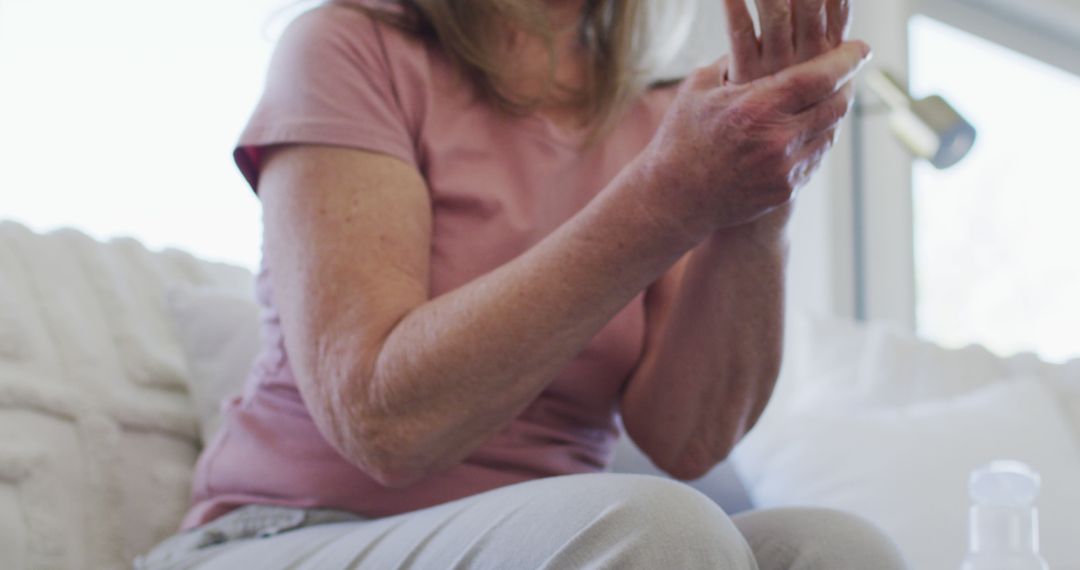 Middle-aged woman applying hand lotion on couch - Free Images, Stock Photos and Pictures on Pikwizard.com