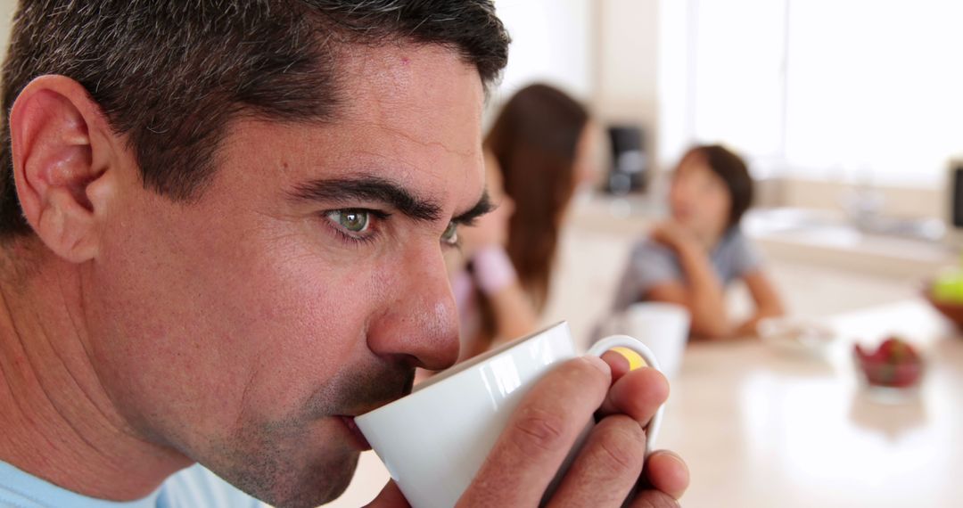 Man Drinking Coffee in Kitchen with Family in Background - Free Images, Stock Photos and Pictures on Pikwizard.com