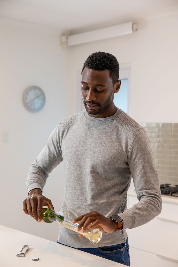 Man Pouring Beverage from Green Bottle in Modern Kitchen