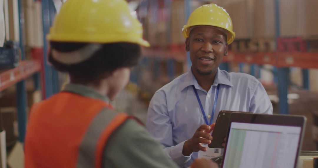 Warehouse supervisor consulting with worker using tablet and laptop in logistics aisle