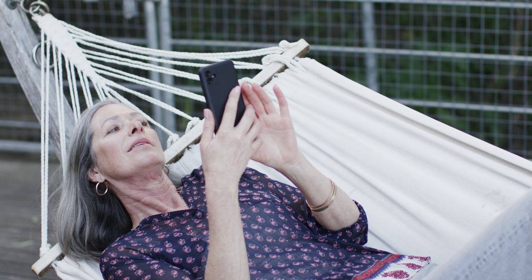 Senior Woman Relaxing in Hammock while Using Smartphone Outdoors - Free Images, Stock Photos and Pictures on Pikwizard.com