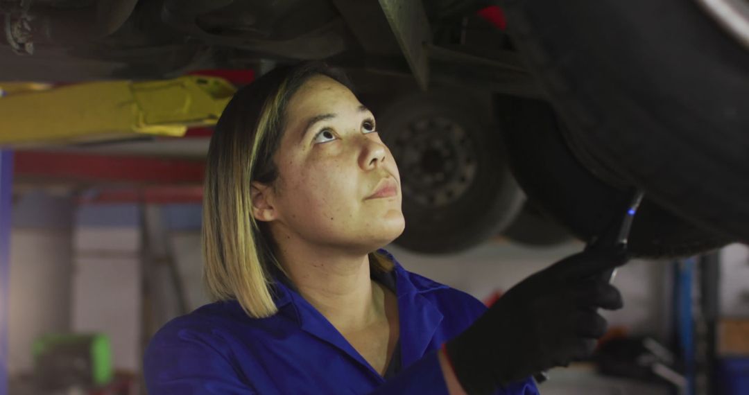 Female Car Mechanic Examining Vehicle Underframe in Workshop