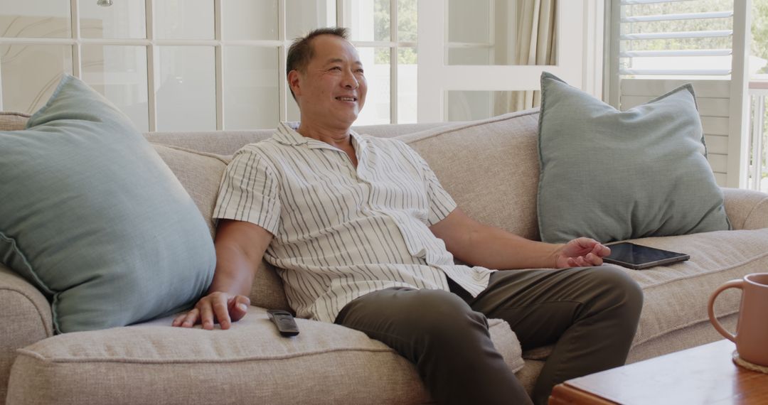 Senior Man Relaxing on Couch with Tablet and Remote Nearby