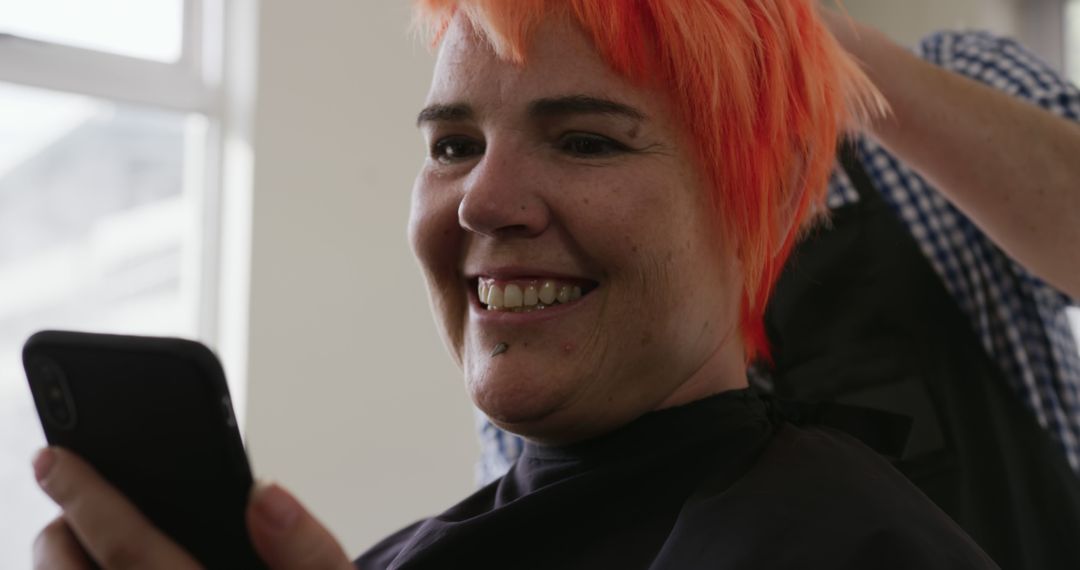 Woman with Bright Orange Hair Smiling and Looking at Mobile Phone in Salon - Free Images, Stock Photos and Pictures on Pikwizard.com