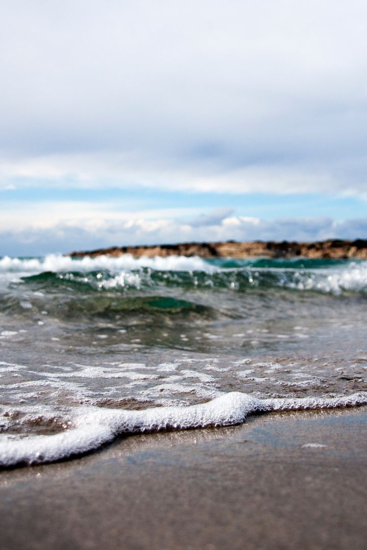 Gentle Waves on Sandy Beach with Distant Hills Under Cloudy Sky