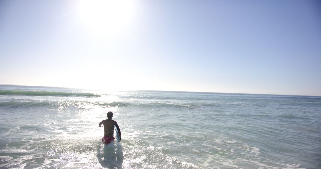 Young Man Entering Sunlit Ocean with Surfboard