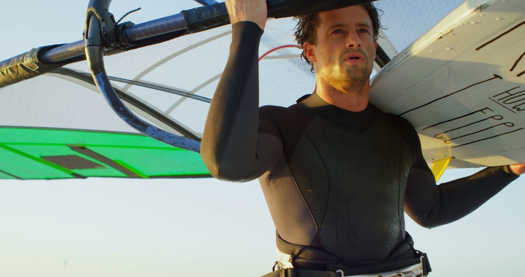 Man Carrying Windsurfing Board on Beach at Sunset - Free Images, Stock Photos and Pictures on Pikwizard.com