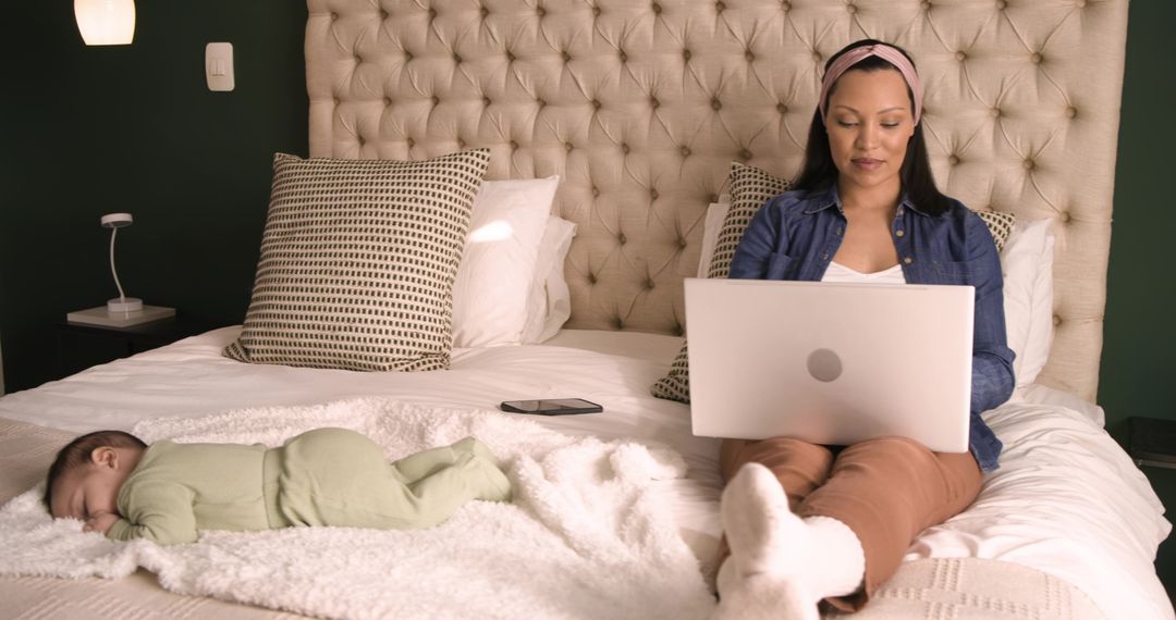 Mother Working Remotely with Sleeping Baby on Cozy Bed