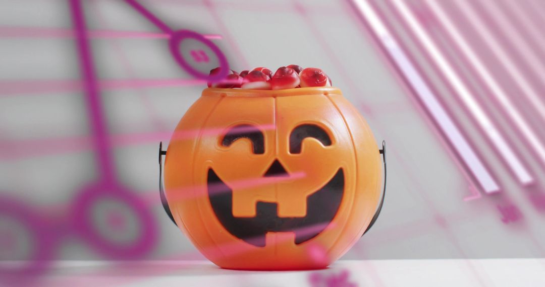 Smiling jack-o'-lantern bucket holding red gummy candies with pink light reflections