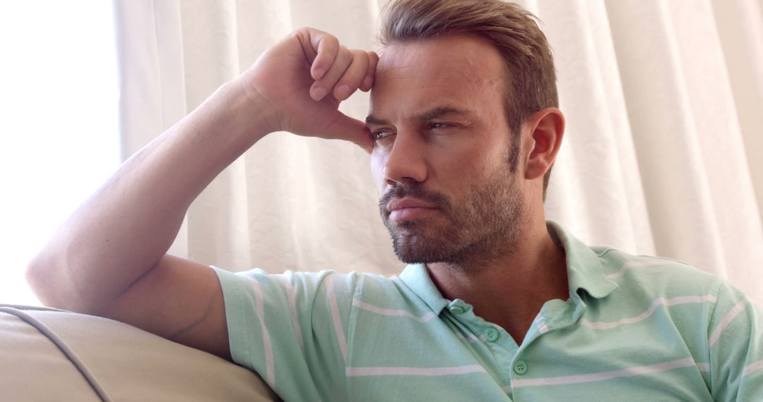 Thoughtful Man Sitting on Sofa with Hand on Forehead - Free Images, Stock Photos and Pictures on Pikwizard.com