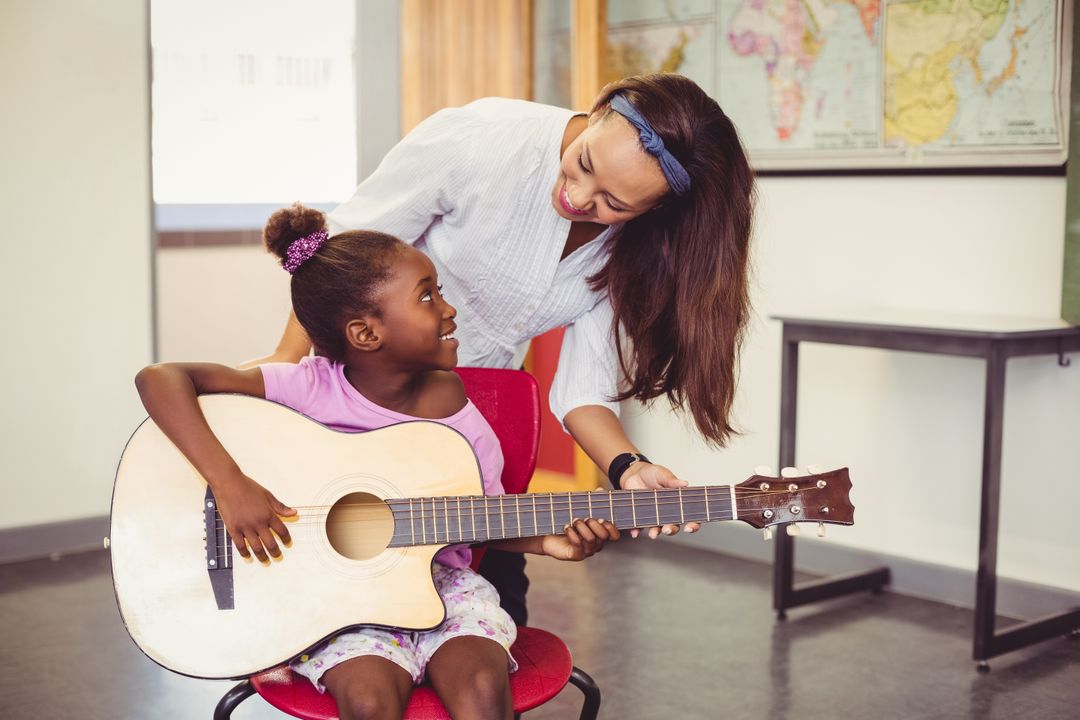 Teacher assisting a girl to play a guitar in classroom - Free Images, Stock Photos and Pictures on Pikwizard.com