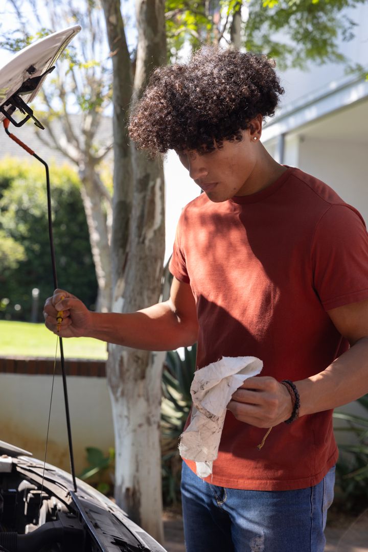 Man Maintaining Car by Checking Oil Levels Outdoors