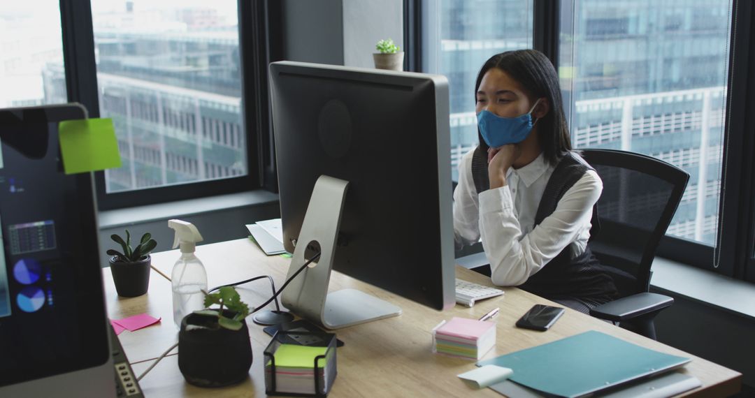 Businesswoman Using Computer and Wearing Face Mask in Modern Office - Free Images, Stock Photos and Pictures on Pikwizard.com