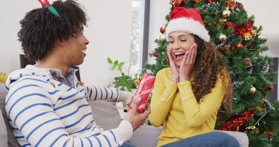 Image of happy diverse couple exchanging christmas gift and embracing at home - Free Images, Stock Photos and Pictures on Pikwizard.com