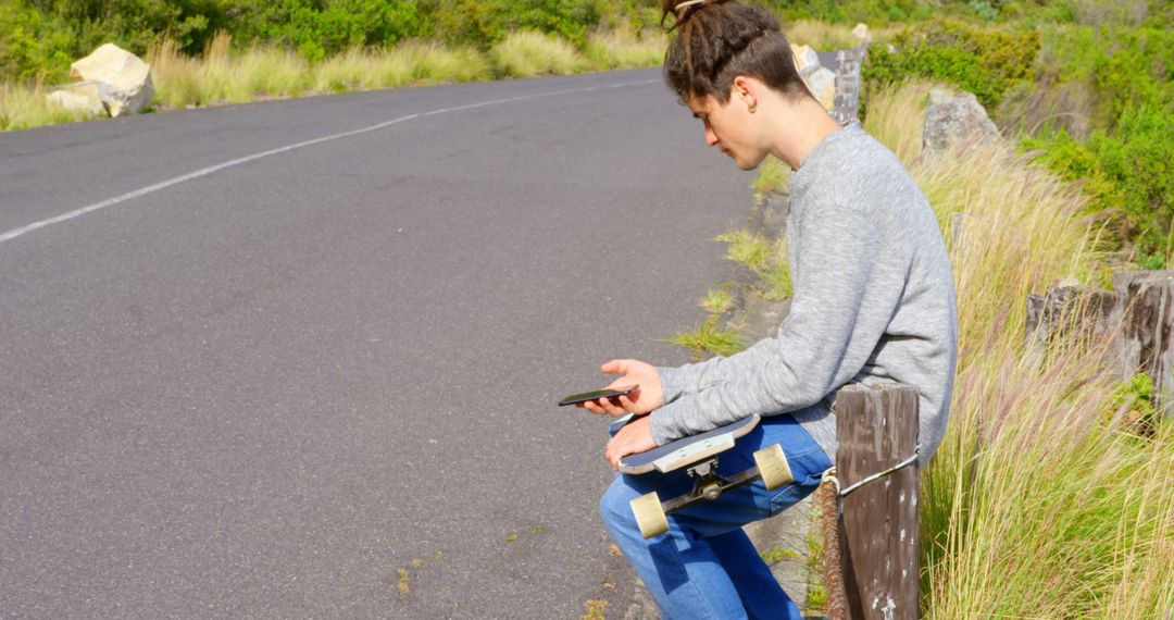 Teen using smartphone while sitting with skateboard in rural area - Free Images, Stock Photos and Pictures on Pikwizard.com