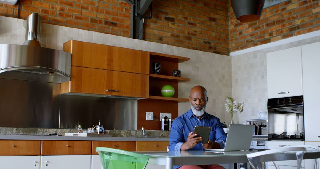 Mature Man Working on Tablet While Sitting in Modern Kitchen - Free Images, Stock Photos and Pictures on Pikwizard.com