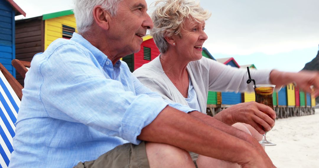 Senior Couple Relaxing on Beach with Colorful Beach Huts - Free Images, Stock Photos and Pictures on Pikwizard.com