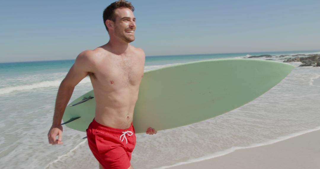 Young Caucasian man holds a surfboard on the beach, with copy space - Free Images, Stock Photos and Pictures on Pikwizard.com