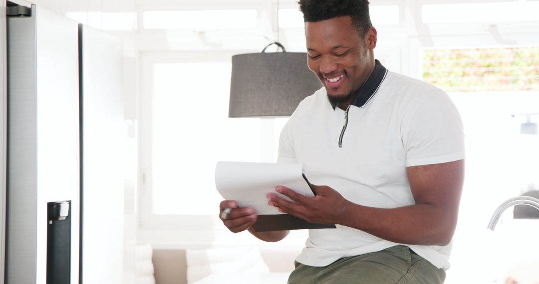 Smiling Man Writing on Clipboard in Modern Kitchen