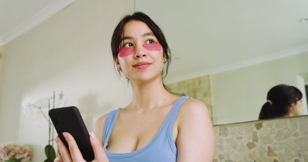 Woman Using Smartphone with Skincare Eye Patches in Modern Bathroom