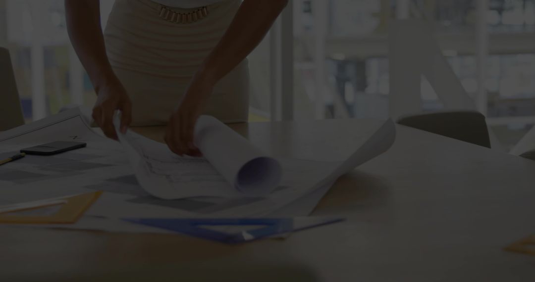 Woman Architect Unrolling Blueprints on Wood Table in Sunlit Studio with Set-Square