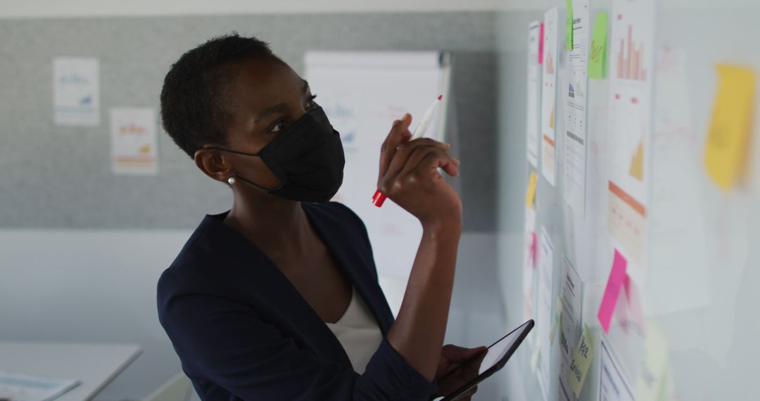 Black Businesswoman in Mask Analyzing Data on Office Wall - Free Images, Stock Photos and Pictures on Pikwizard.com