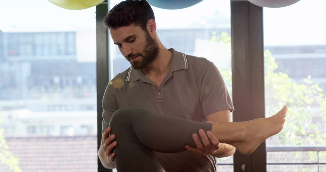 Trainer Supporting Client Leg During Rehabilitation Stretch in Urban Studio Balcony