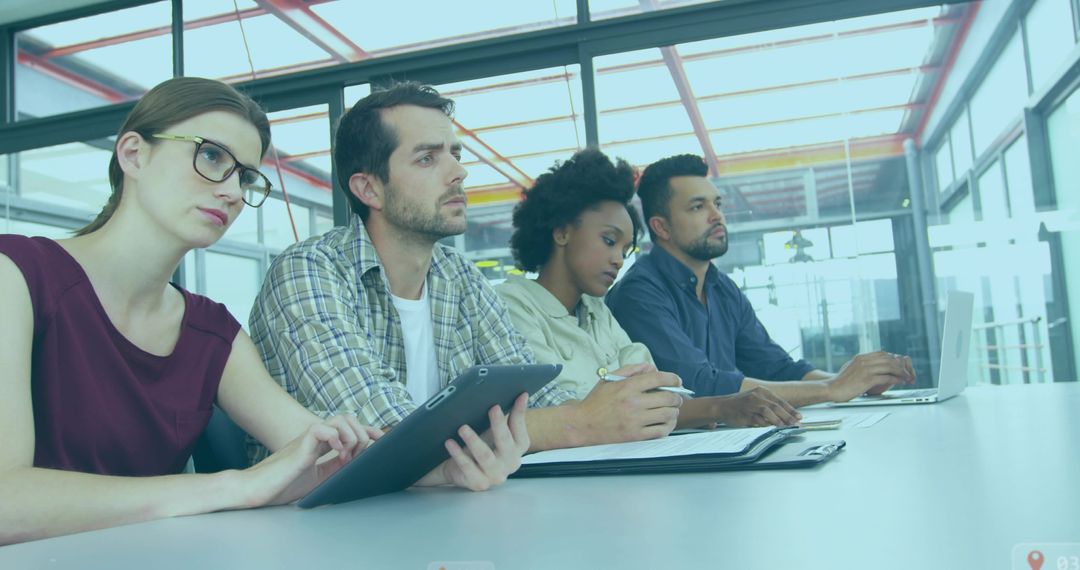 Diverse team listening and taking notes in modern glass meeting room with devices