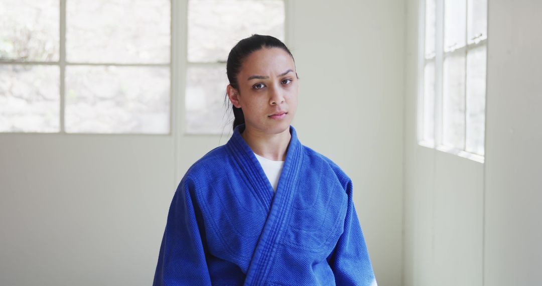 Confident Young Woman in Blue Martial Arts Uniform Standing Indoors - Free Images, Stock Photos and Pictures on Pikwizard.com