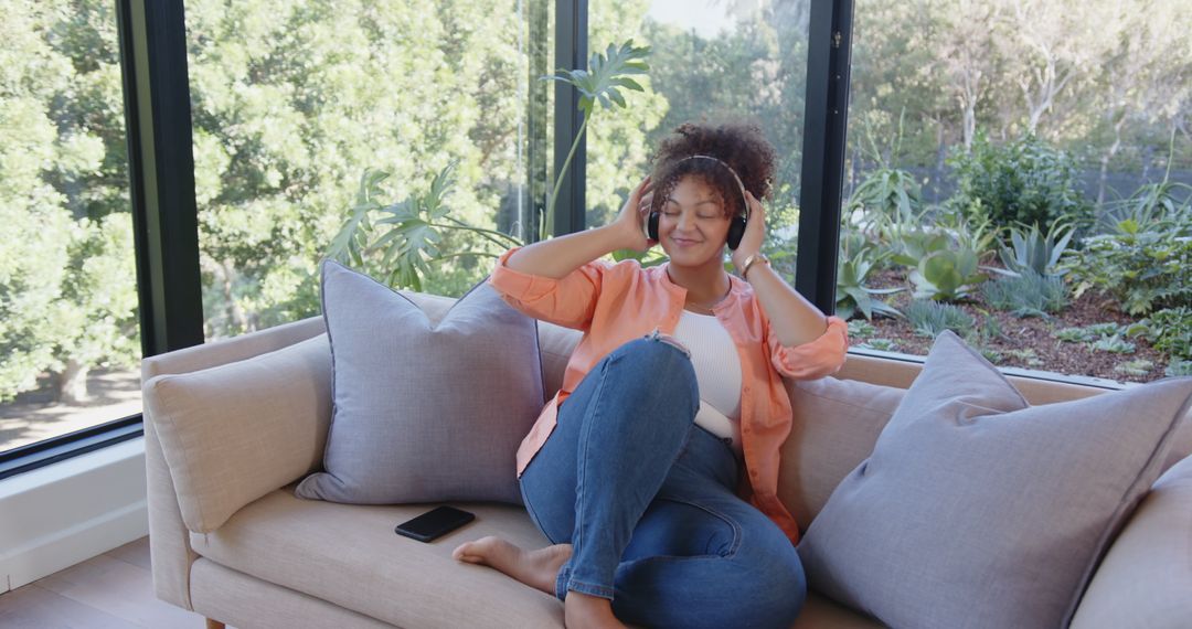 Woman Enjoys Music on Sofa Near Large Windows at Home