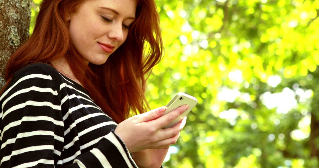 Smiling Young Woman Texting on Smartphone in Outdoor Park - Free Images, Stock Photos and Pictures on Pikwizard.com