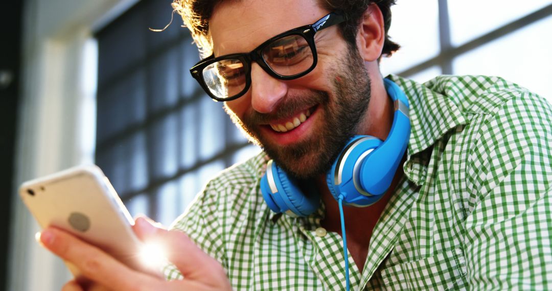 Young Man Smiling While Using Smartphone and Wearing Headphones - Free Images, Stock Photos and Pictures on Pikwizard.com