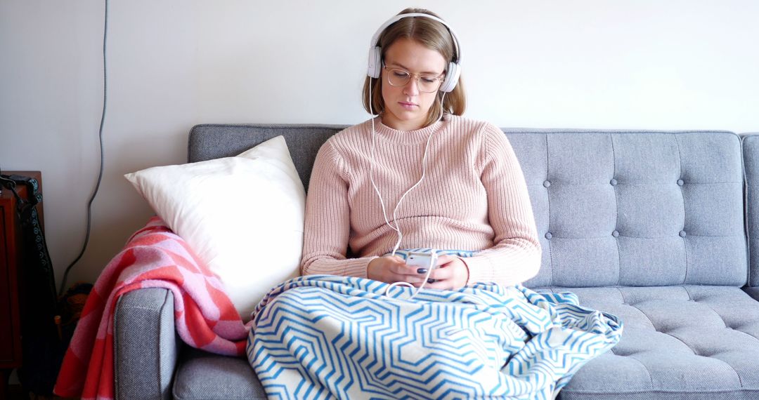 Woman Relaxing on Sofa with Blanket and Headphones, Browsing Smartphone - Free Images, Stock Photos and Pictures on Pikwizard.com