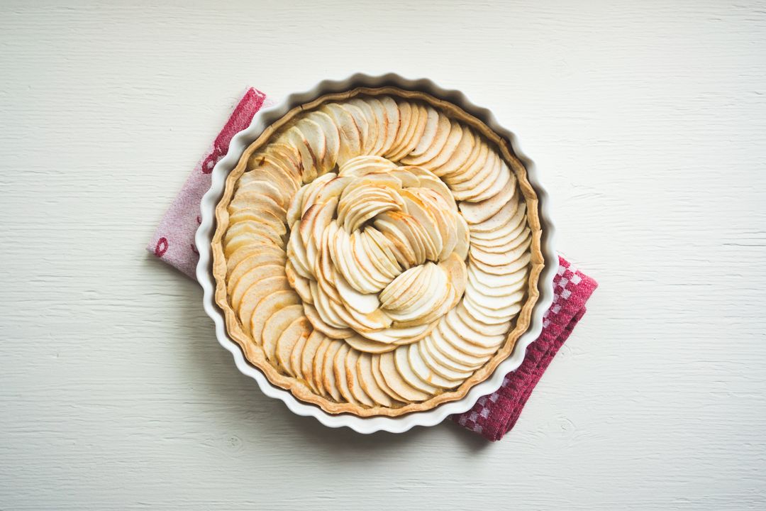 Rustic apple tart showcasing concentric layers of thinly sliced apples in white fluted tart pan