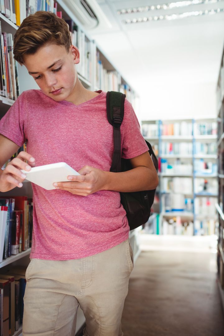 Teen Boy Engaged in Learning with Tablet in Library Aisle