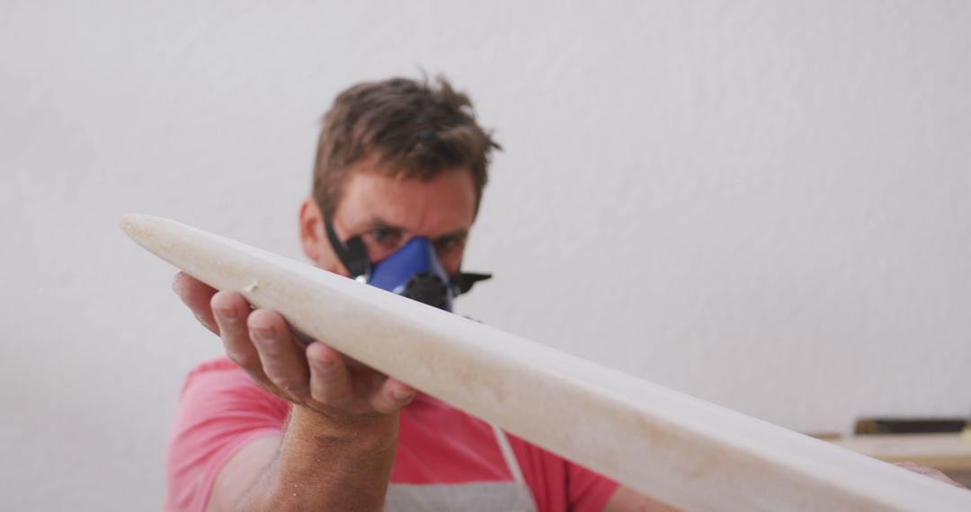 Carpenter shaping wooden surfboard wearing safety mask - Free Images, Stock Photos and Pictures on Pikwizard.com